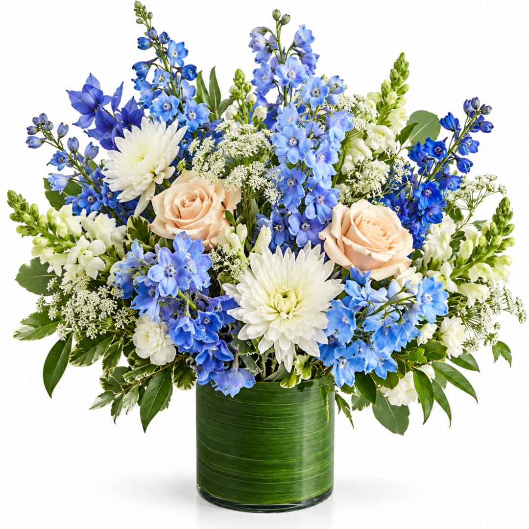 Blue and white floral arrangement with peach roses in a green glass vase