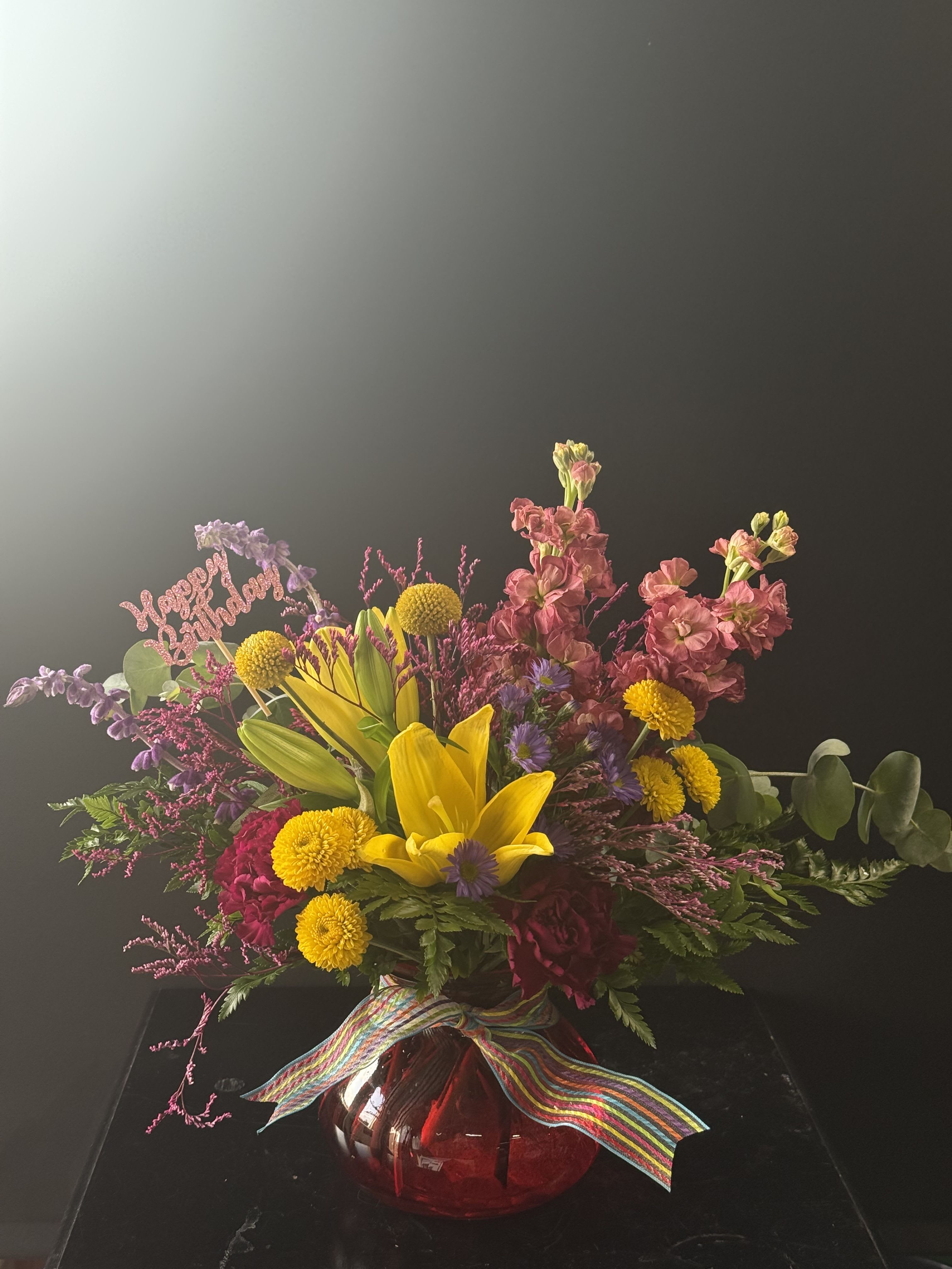 Colorful mixed bouquet in a red glass vase with a rainbow ribbon