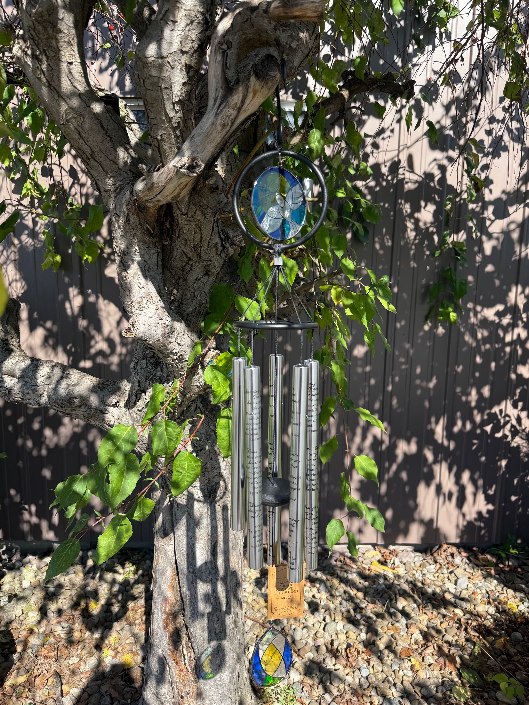 Stained-glass and metal wind chime hanging from a tree branch