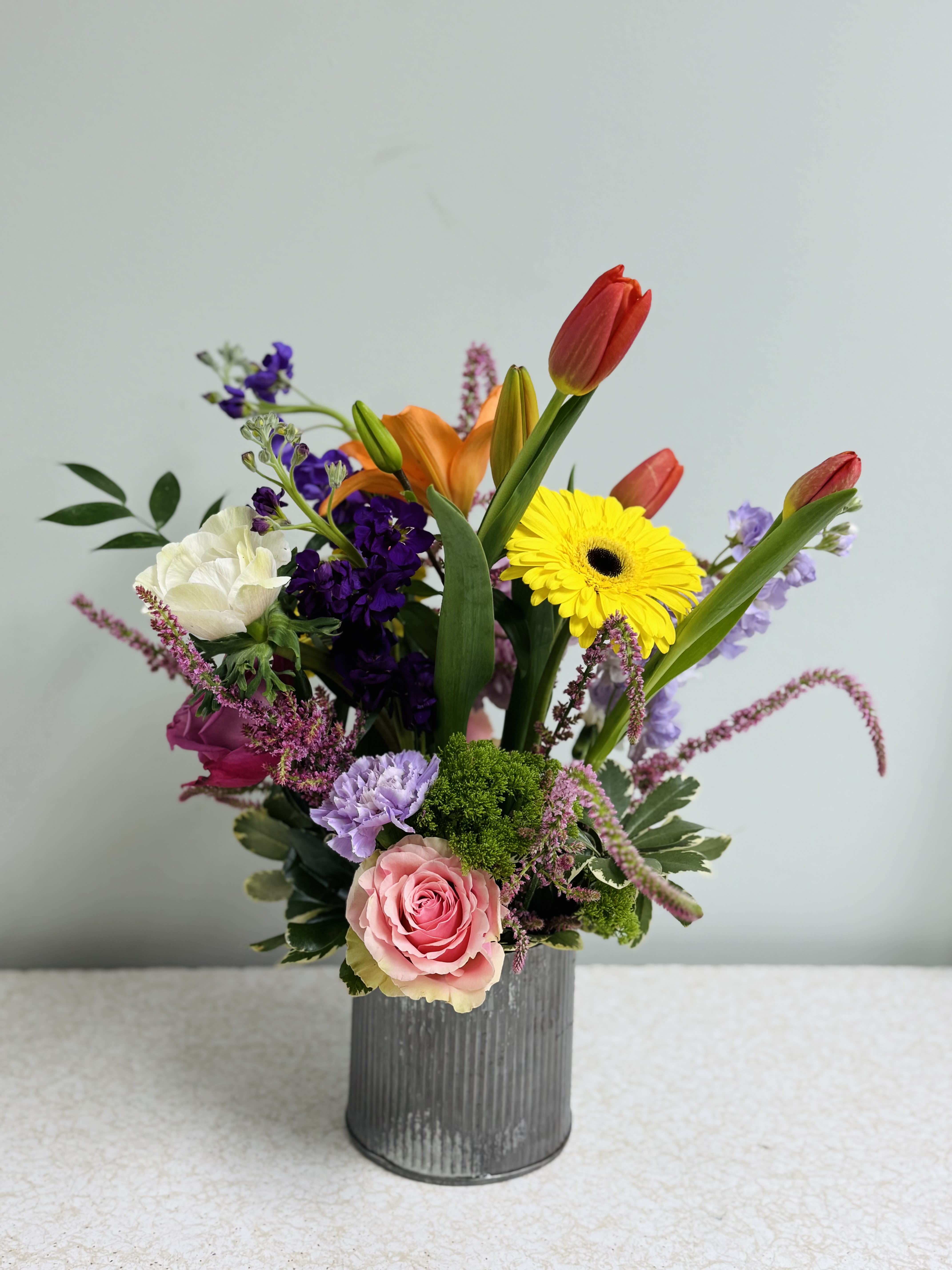 Mixed bouquet in a gray vase with tulips, roses, and a yellow gerbera daisy
