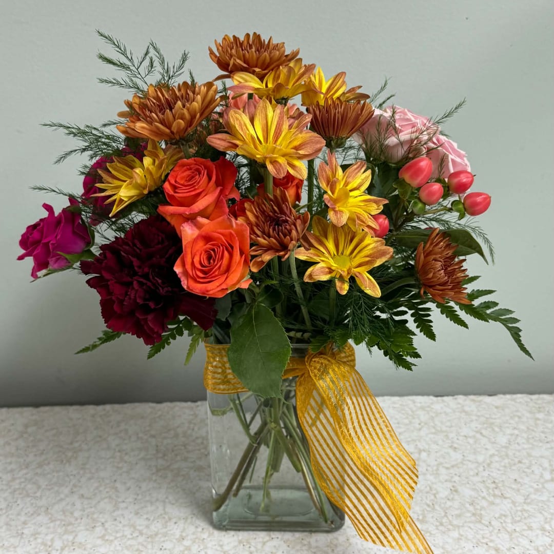 Mixed bouquet of roses and chrysanthemums in a glass vase with a yellow ribbon