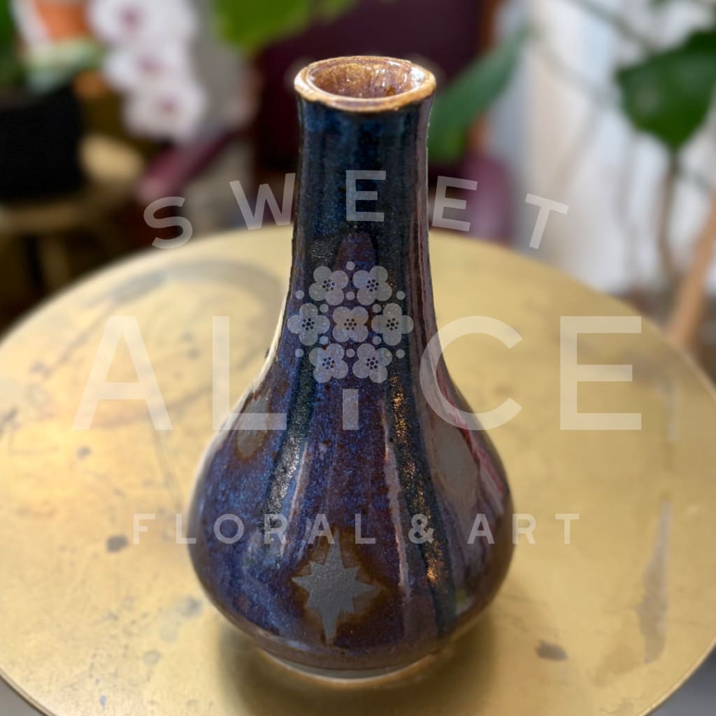 Small dark blue ceramic vase with a narrow neck on a round table