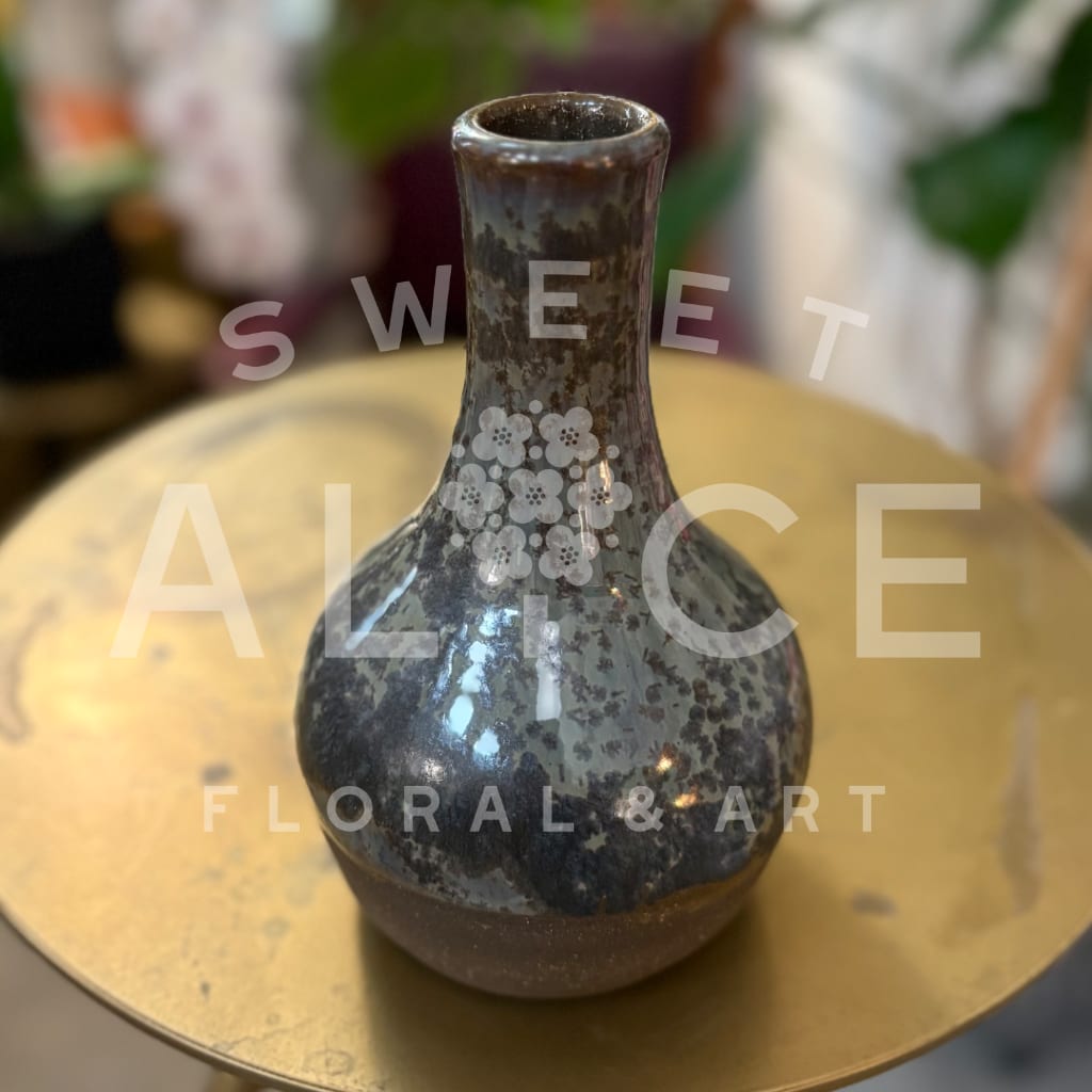 Small dark ceramic vase with a floral pattern on a gold tray