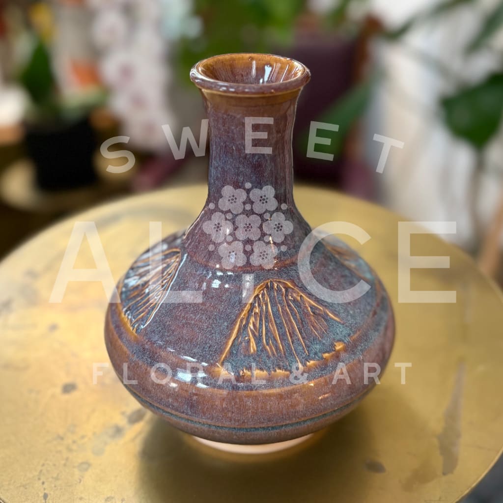 Brown ceramic vase with etched floral patterns on a round table