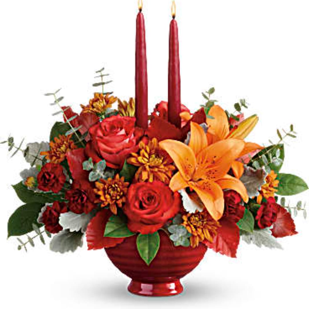 Red and orange floral arrangement in a red vase with two tall candles