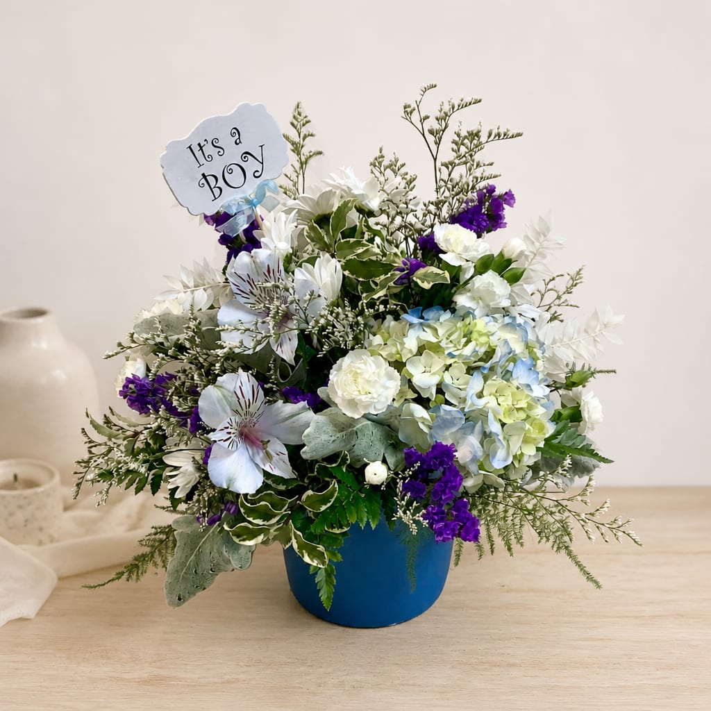 White and purple floral arrangement in a blue pot with a "It's a Boy" sign