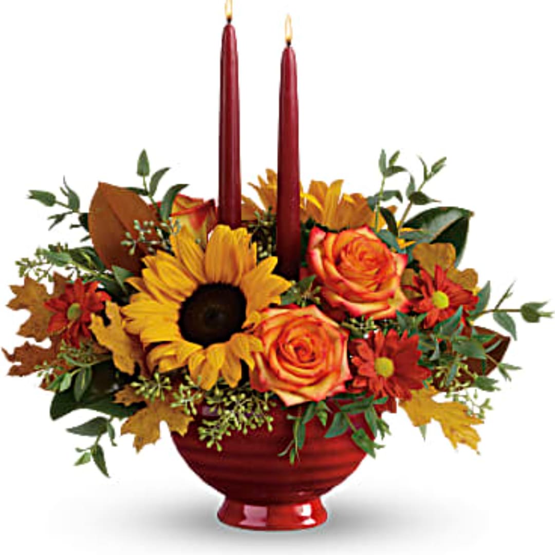 Autumn floral arrangement with sunflowers, roses, and two red taper candles in a red bowl