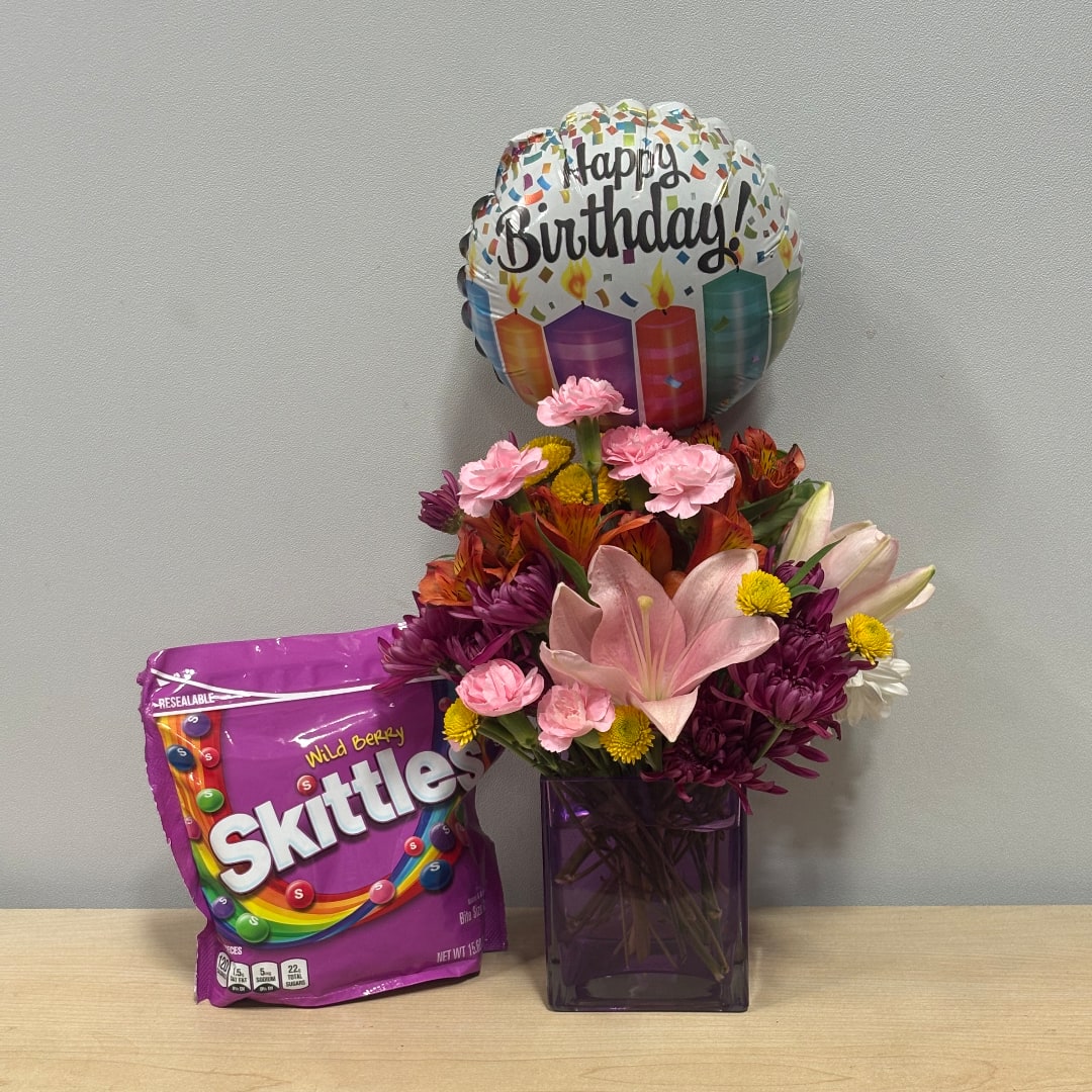 Birthday balloon above a mixed flower arrangement with a candy bag beside it