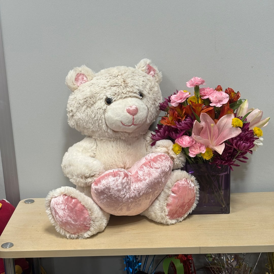 Teddy bear beside a mixed bouquet in a purple vase