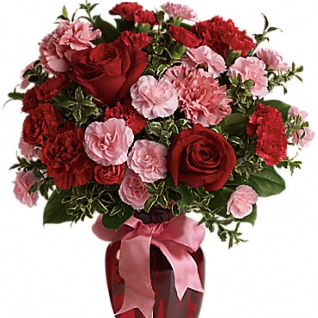 Red roses and pink carnations arranged in a vase with a pink ribbon