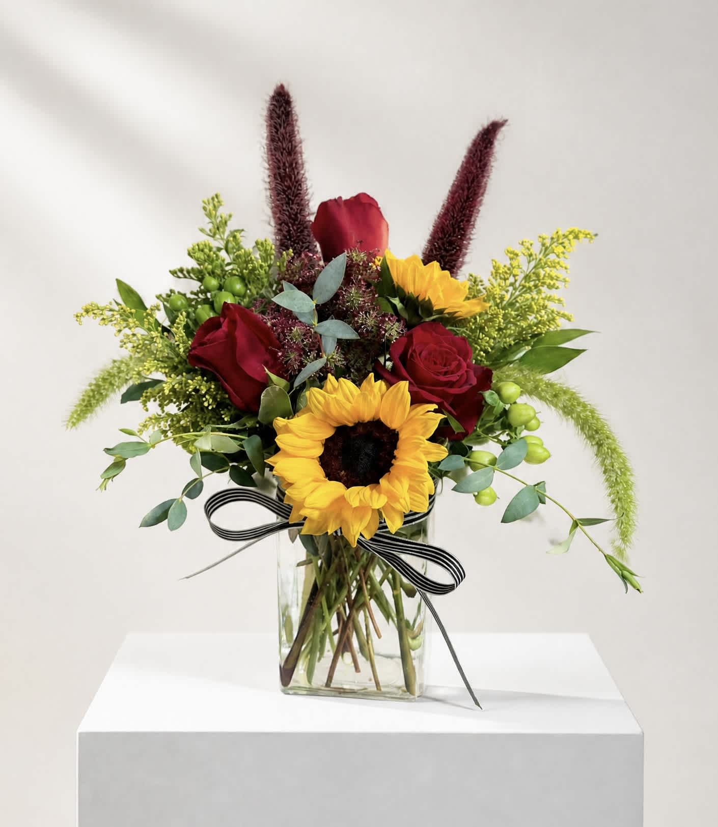 Bouquet of red roses and sunflowers in a glass vase with a striped ribbon