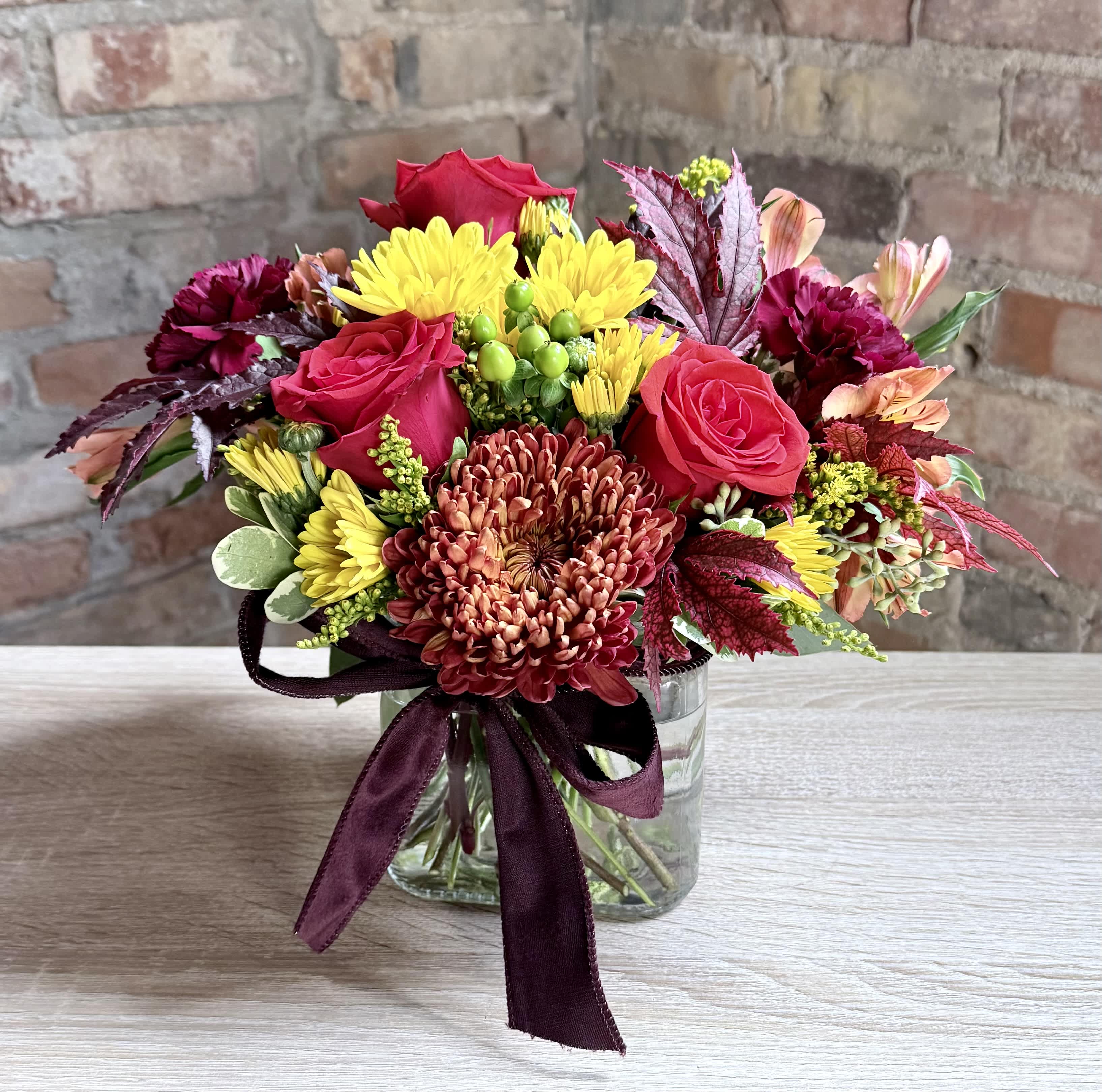 Bouquet of red roses and yellow chrysanthemums in a glass vase with a burgundy ribbon
