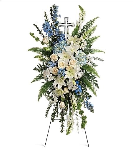 Standing floral spray with white lilies, blue flowers, and a cross