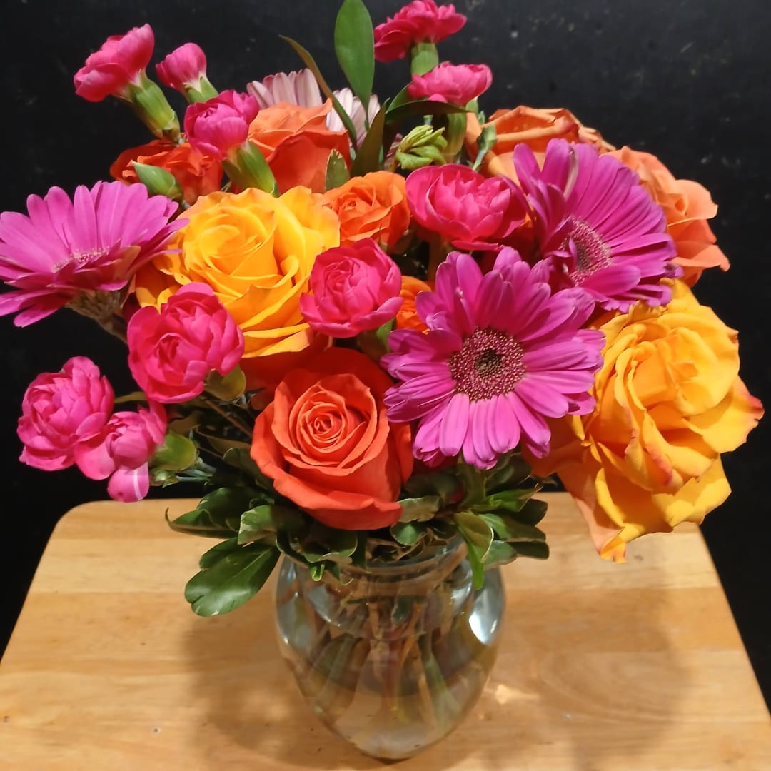 Mixed bouquet of pink, orange, and yellow flowers in a glass vase