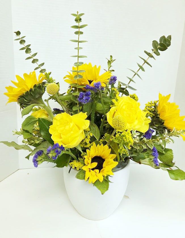 Yellow sunflowers and purple filler flowers in a white vase