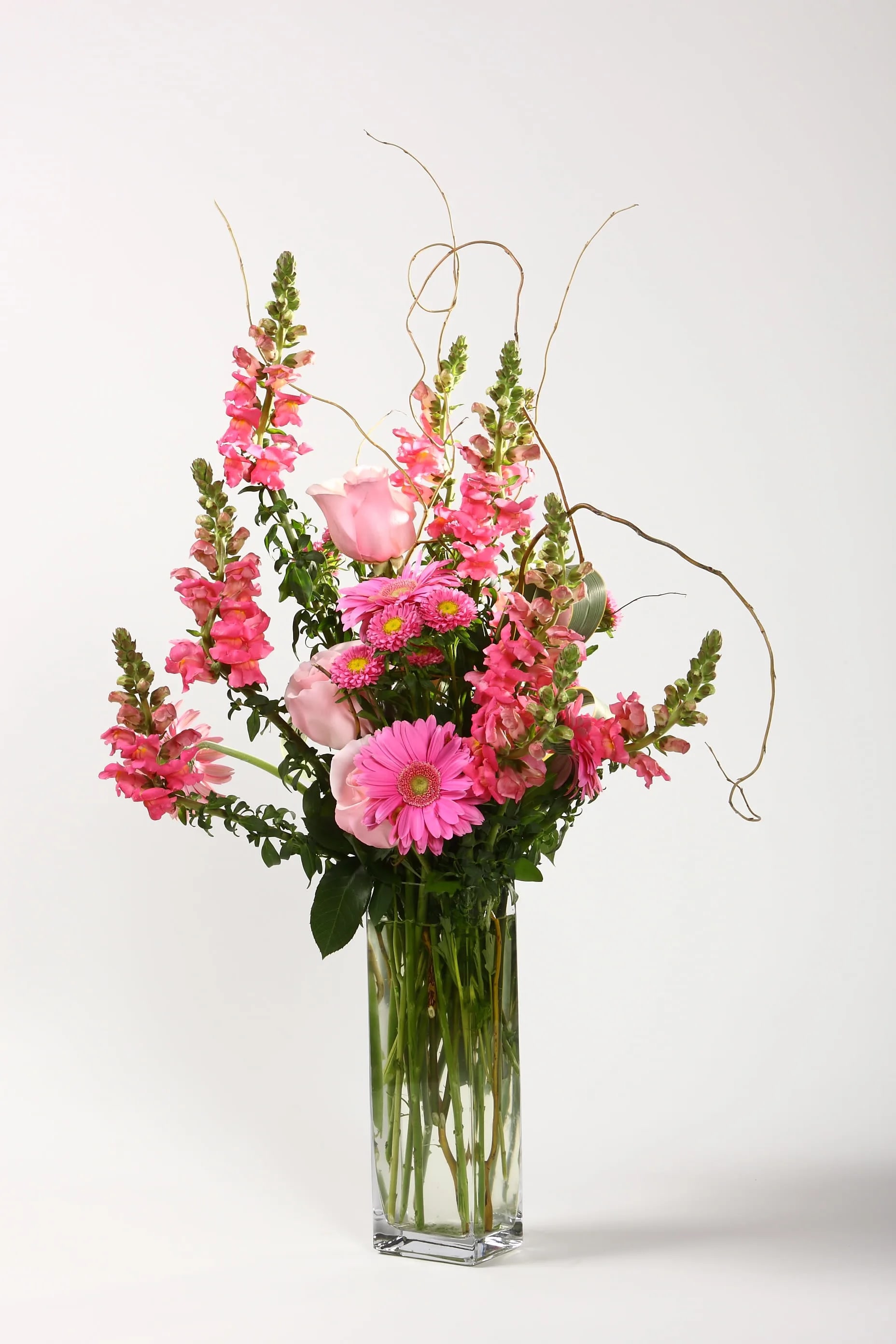 Pink flowers arranged in a tall clear glass vase with curly branches
