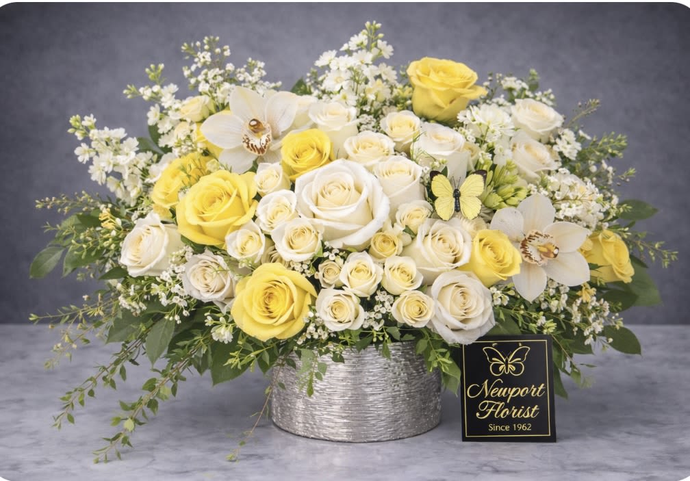 Garden in Elegance - A bright, cheerful bouquet of yellow and white roses creates an instant moment of celebration-perfect as a birthday bouquet, springtime gift, or to mark an anniversary. Rounded and abundant, the arrangement reads as both elegant and playful: the delicate mix of roses and small white filler flowers frames airy greenery and whimsical decorative butterfly picks that catch the eye and lift the design.  Arranged in a textured silver container, the flowers form a dense, polished centerpiece that's gift-ready the moment it arrives. The palette of white, yellow and fresh green feels sunny without being overpowering; petals are tightly clustered for a full visual impact while softer greenery and filler flowers soften the silhouette. A small florist sign completes the presentation, adding a thoughtful finishing touch.  This is the kind of arrangement that makes the person you're thinking of feel genuinely celebrated-cheerful, noticed, and appreciated. Available in a single rounded size; keep blooms fresh by changing the water every two days and trimming stems slightly when you refresh the vase.