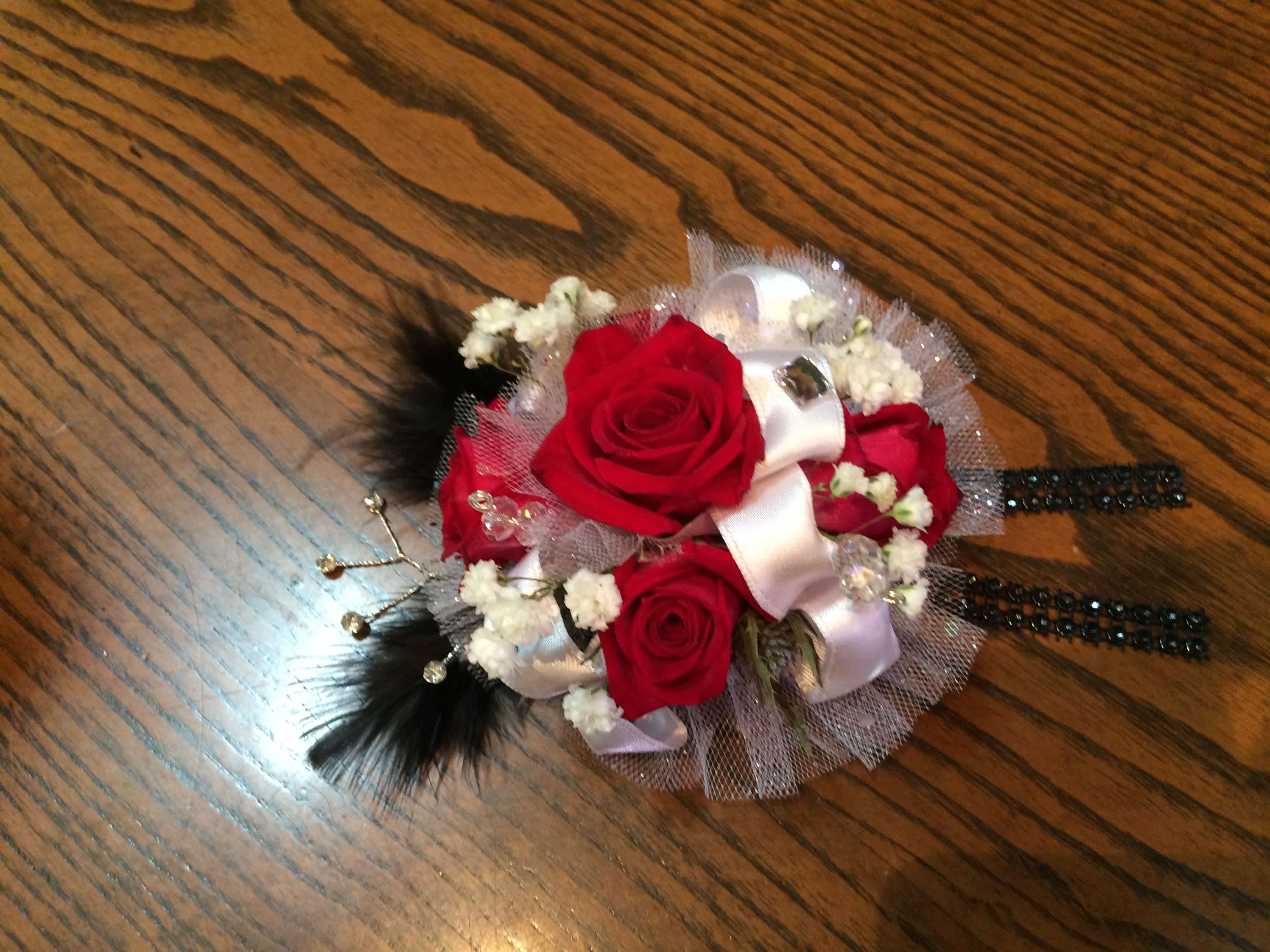 Red rose corsage with white ribbon and black feather accents