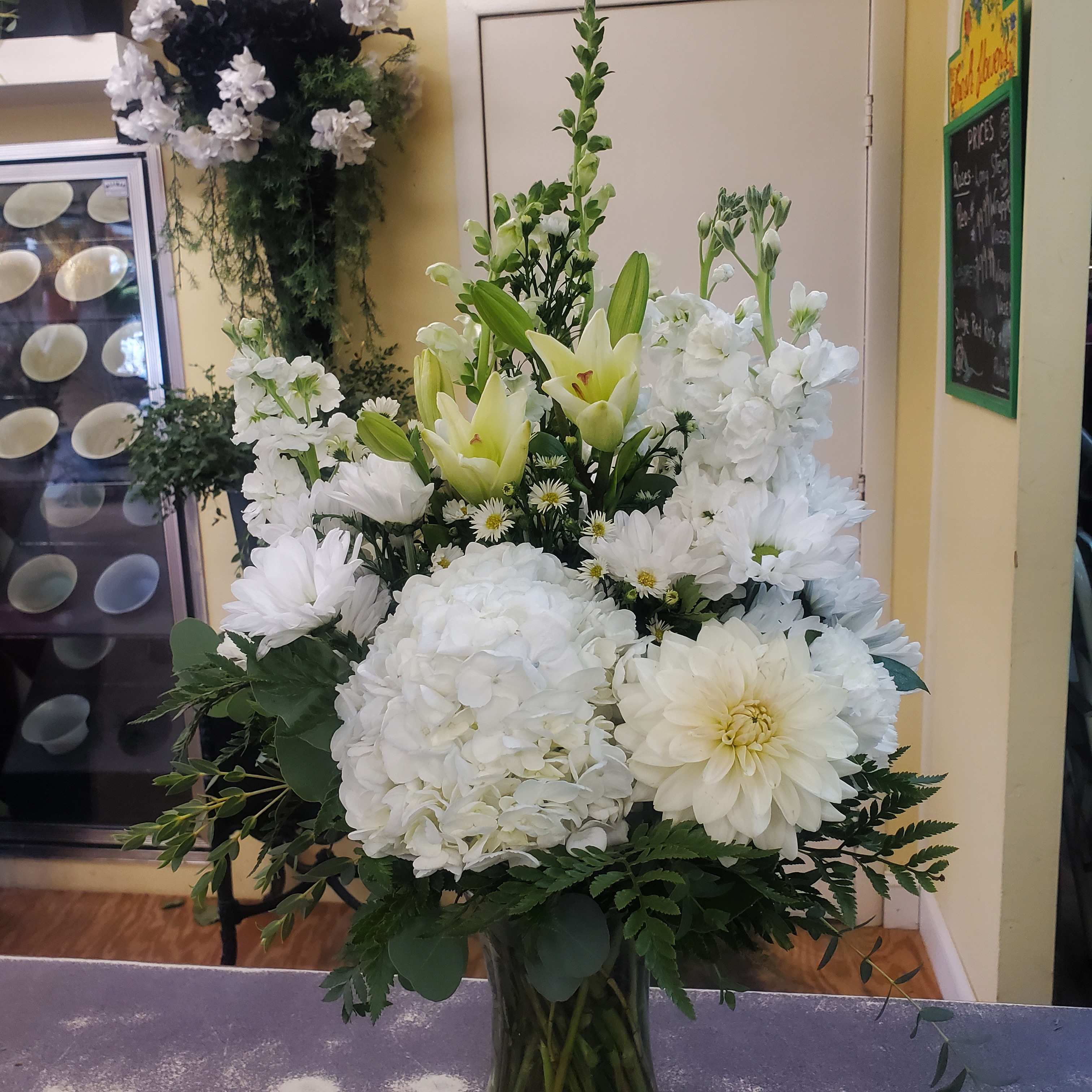 Tall white floral arrangement with lilies, hydrangeas, and daisies in a glass vase