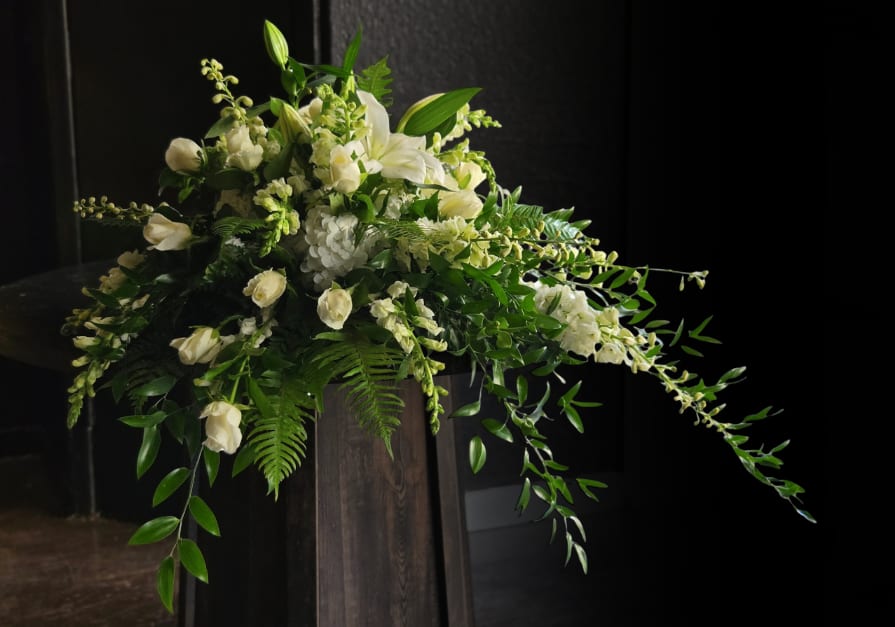 White floral arrangement with cascading greenery on a dark pedestal