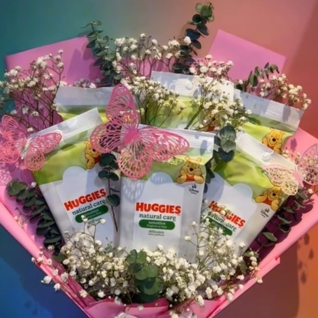 Baby care packs arranged in a pink bouquet with small white flowers and butterfly decorations