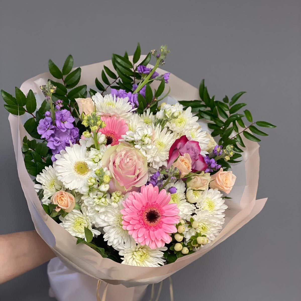 Hand-tied bouquet of pink, white, and purple flowers wrapped in pale paper