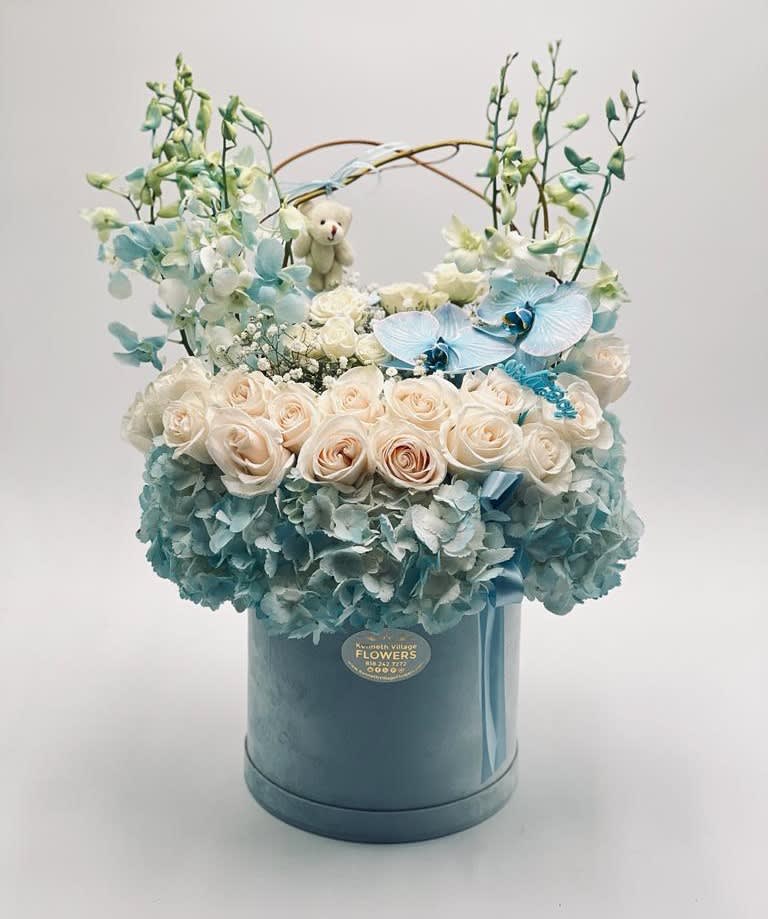 Blue and white floral arrangement in a round hatbox with a small teddy bear