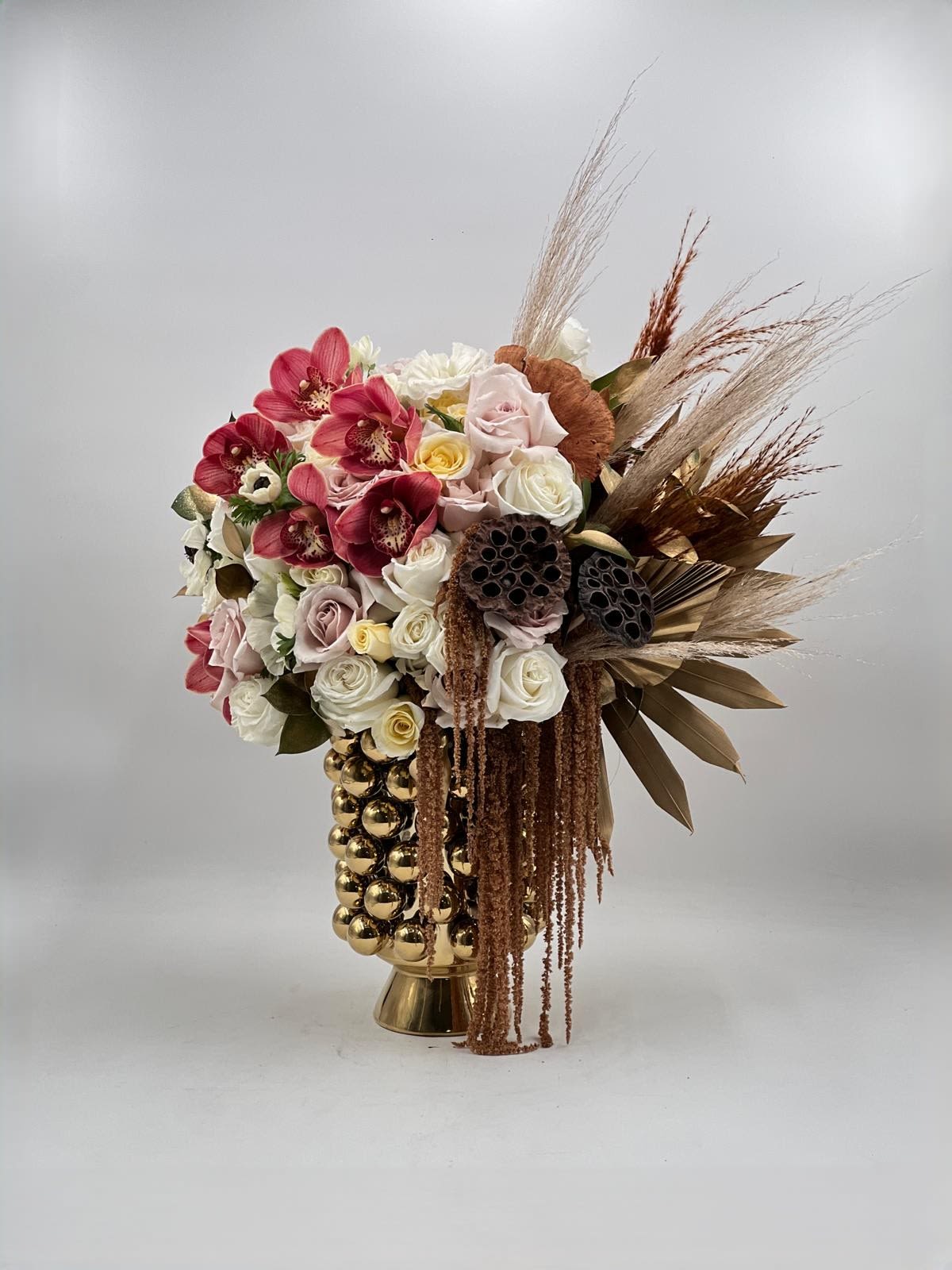 Bouquet of pink and white roses with dried grasses in a gold vase