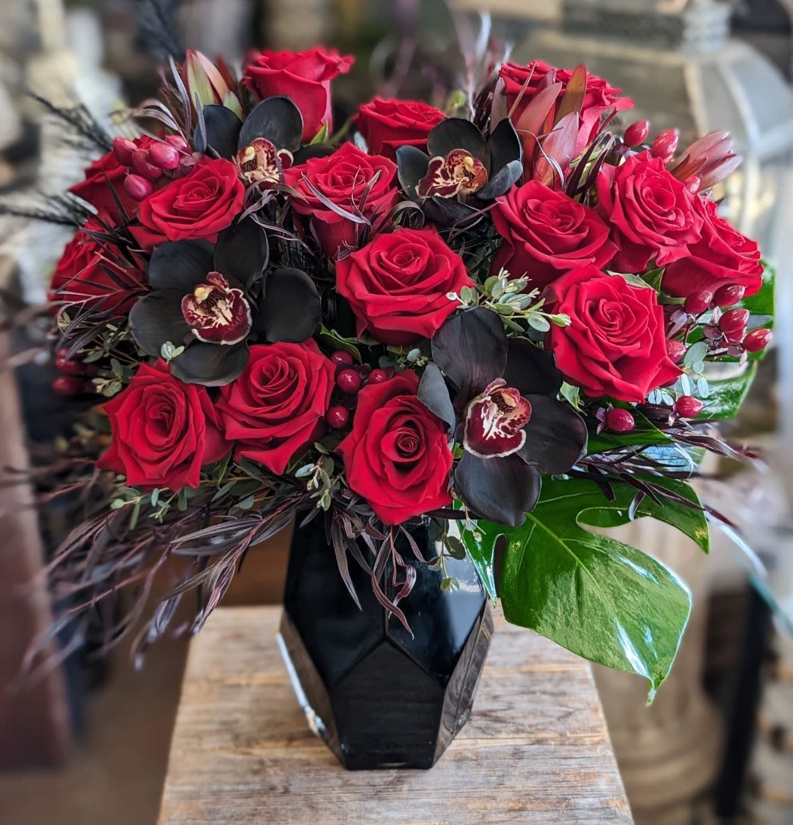 Red roses arranged in a black geometric vase with dark orchids