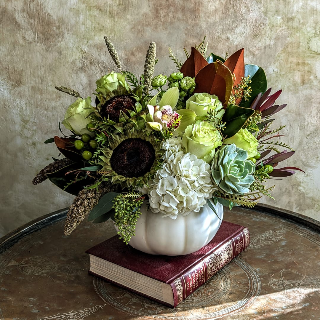 Mixed floral arrangement in a white pumpkin-shaped vase on a book