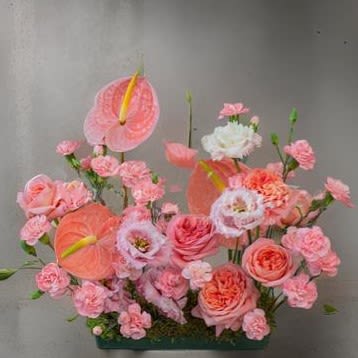 Pink floral arrangement with anthuriums, roses, and carnations in a low container