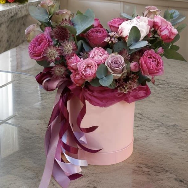 Pink and lavender roses in a round hatbox with ribbon