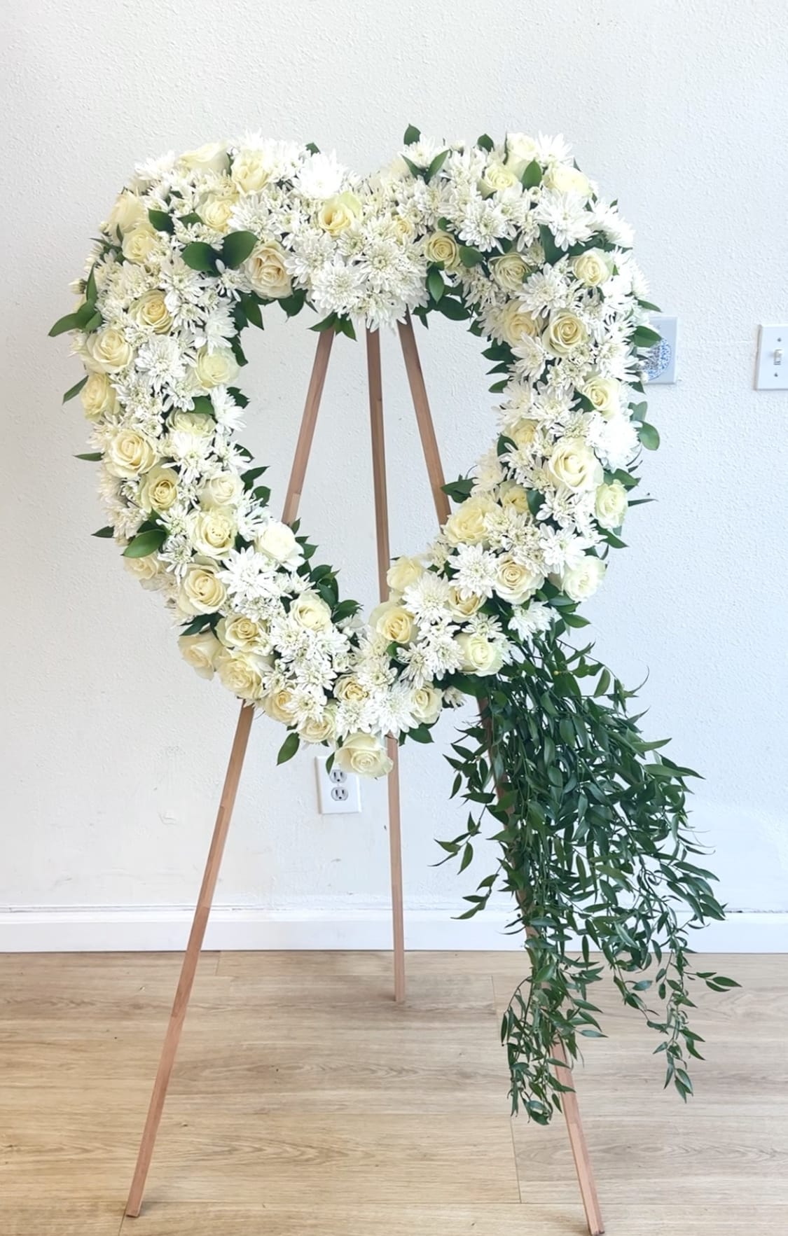 Heart-shaped white floral wreath on a wooden easel with trailing greenery