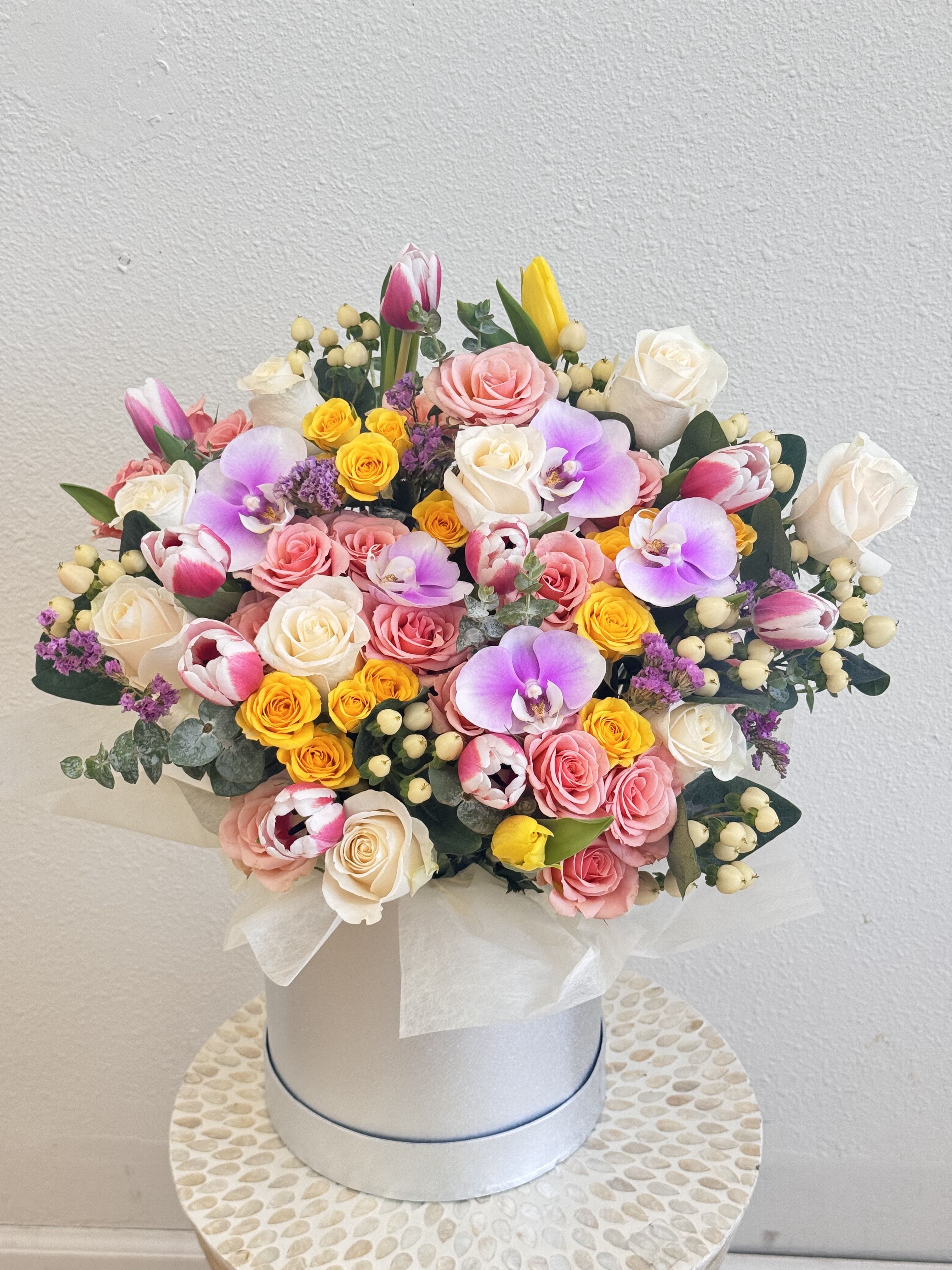 Mixed bouquet of roses, tulips, and orchids in a white hat box