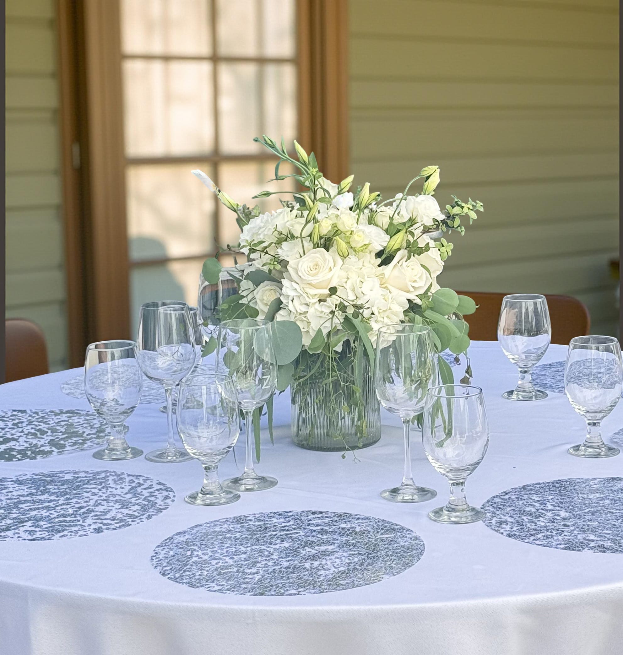 White floral centerpiece in a glass vase on a round table with wine glasses