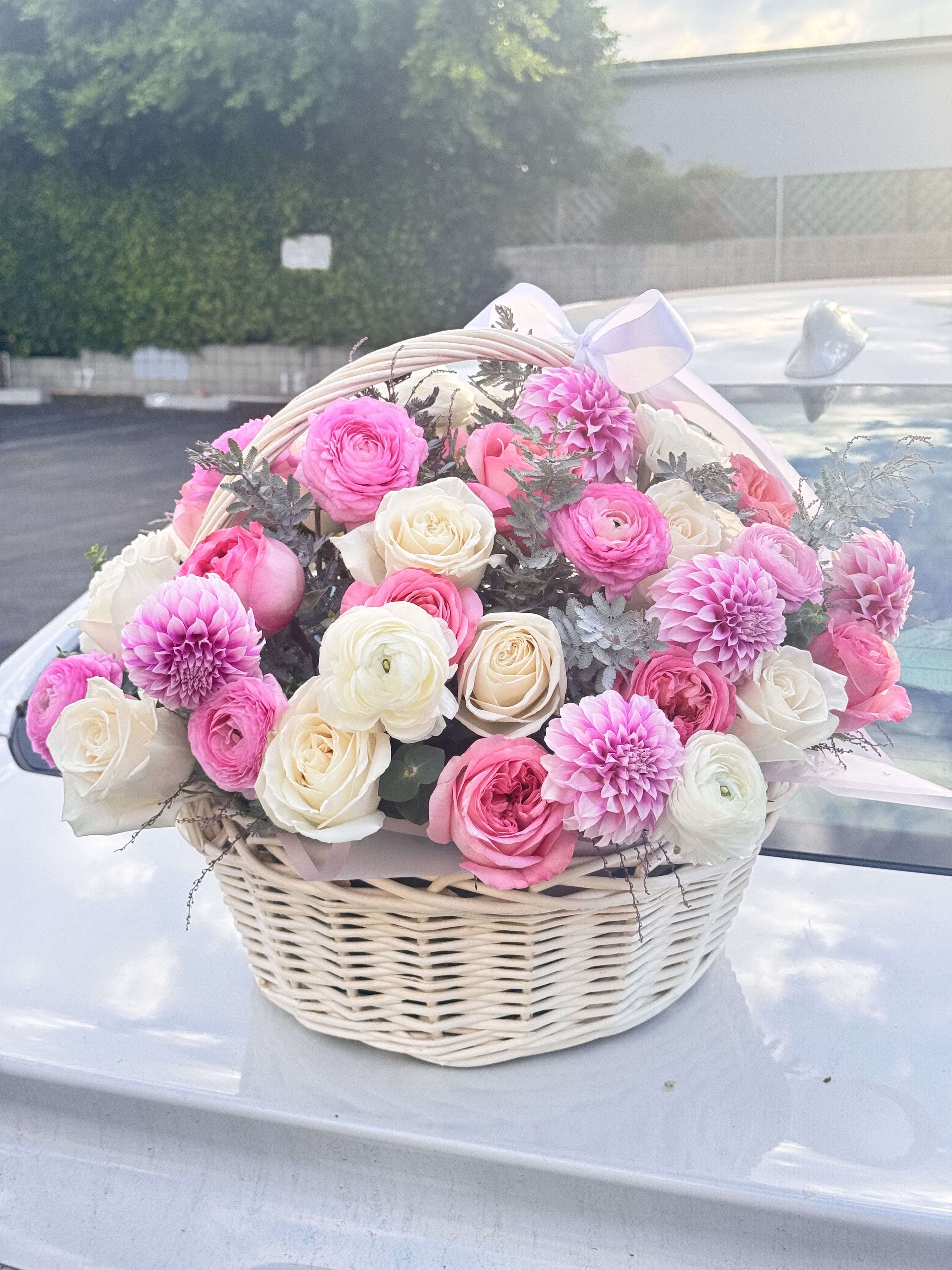 Pink and white flowers arranged in a wicker basket with a ribbon bow