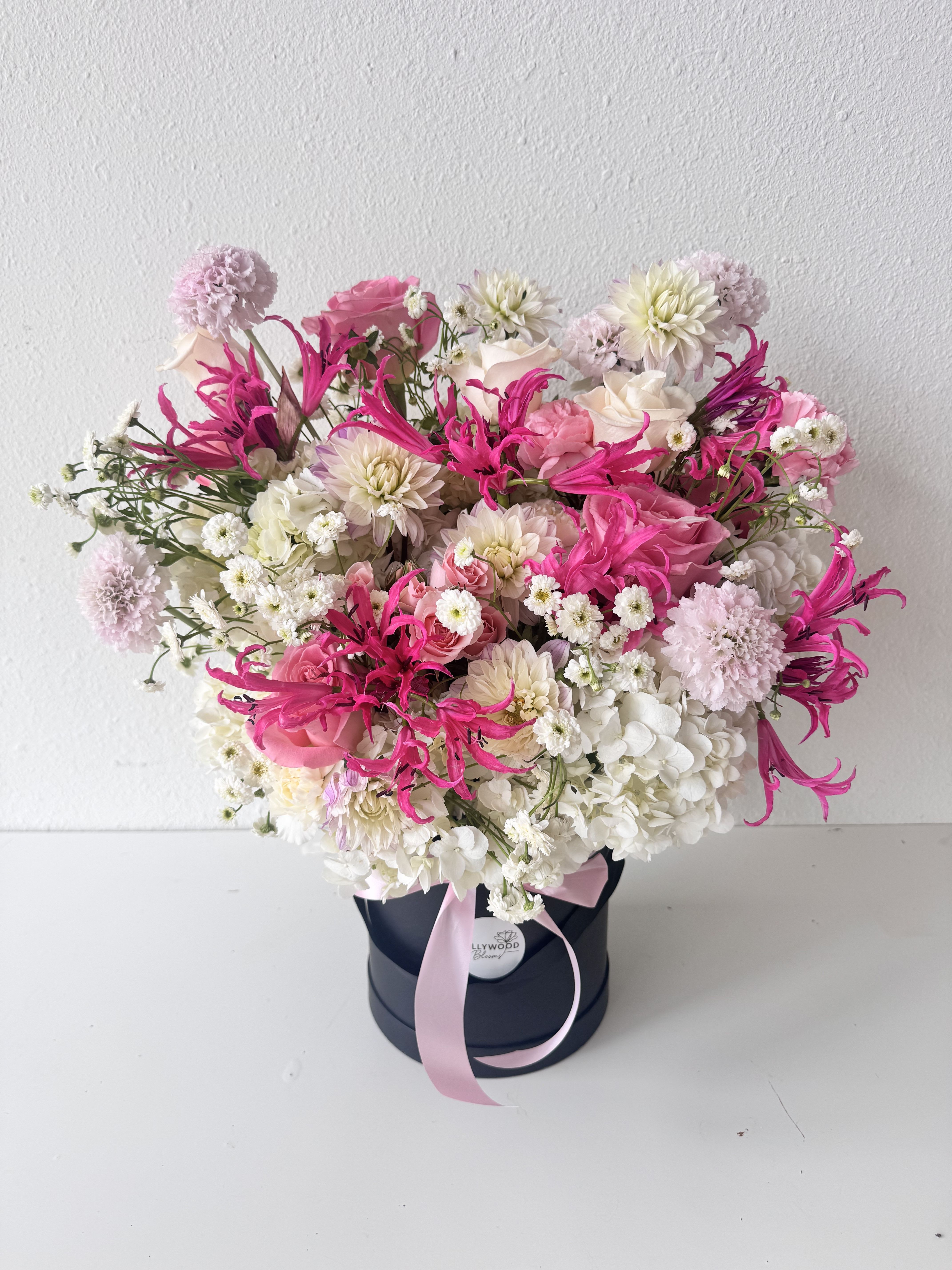 Pink and white mixed flower arrangement in a black hat box with a ribbon
