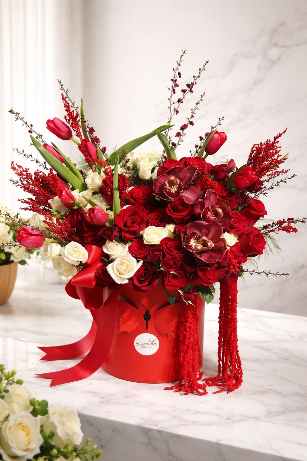 Red and white rose arrangement with tulips in a red hatbox