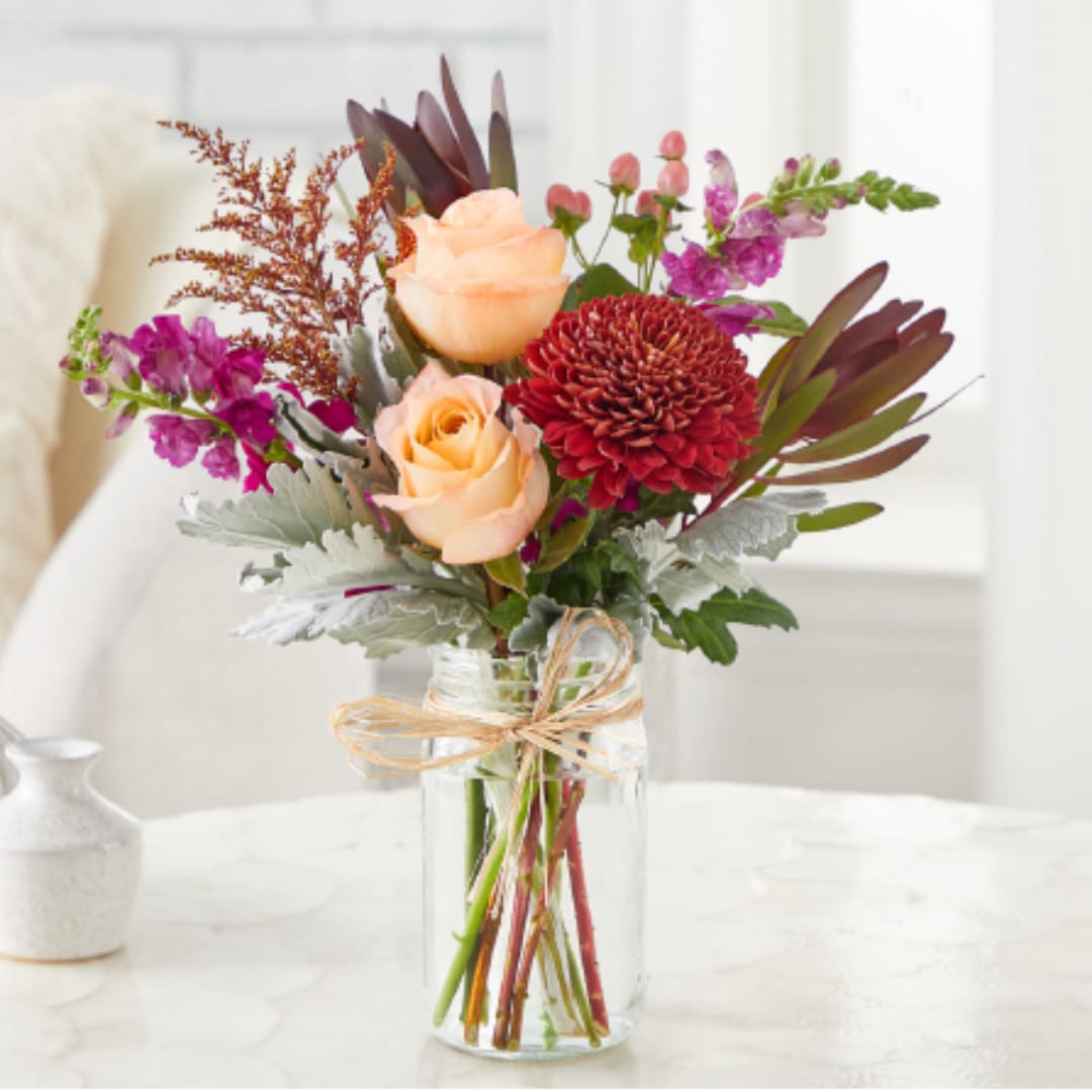 Bouquet of peach roses and red mums in a clear glass vase