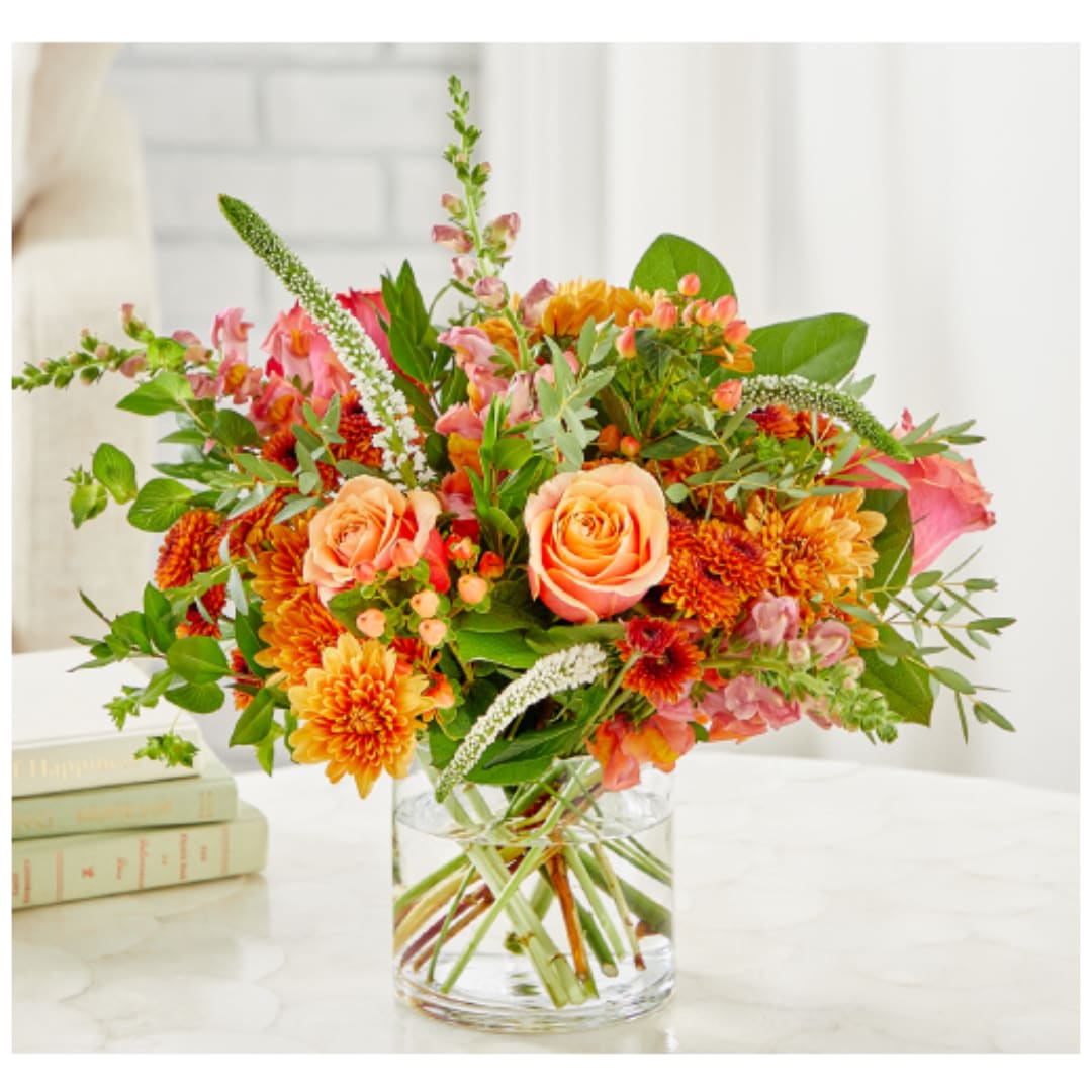 Mixed bouquet of peach roses and orange blooms in a clear glass vase