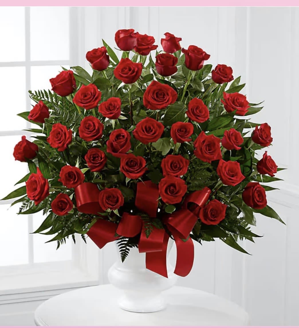 Large arrangement of red roses with red ribbon in a white pedestal vase