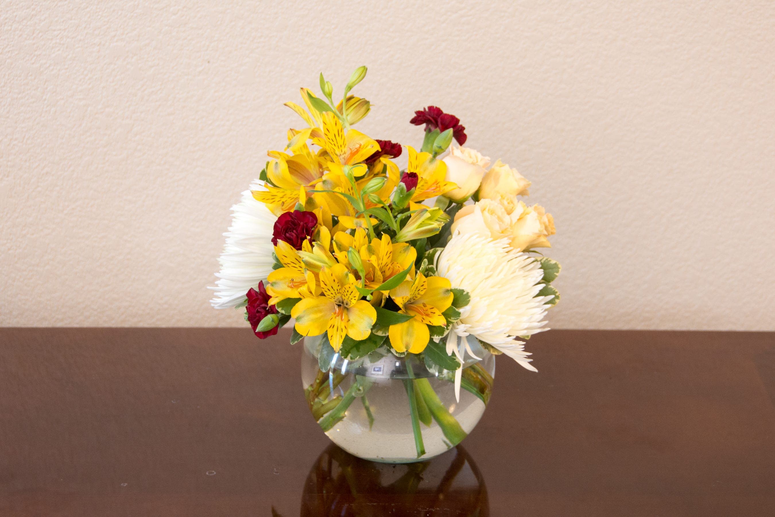 A Touch of Color - Mixed Color Compact Bouquet in Clear Vase (Birthday, Thank You) - Bright, compact and unexpectedly cheerful, this mixed color compact bouquet in a clear glass vase is a perfect birthday or thank-you gift that will make the person you're thinking of smile. The arrangement reads as both uplifting and gently romantic, making it equally well suited for get well wishes, thinking of you moments. Its rounded, low silhouette fits neatly on a bedside table, office desk, or kitchen counter and carries a fresh, hand-arranged feel that works year-round. The bouquet blends white hydrangeas or white chrysanthemums as a soft, cloudlike base with roses and carnations for bold accents.  Alstroemeria adds delicate, speckled texture while spray roses weave through the mix for extra depth. Some variations  vivid blue spikes for a red-white-blue patriotic touch - all gathered tightly in a round clear glass bowl vase.  Choose this bouquet to brighten a recovery room, celebrate a birthday, say thank you, or tell someone they're loved - she'll feel genuinely seen and comforted by the thoughtful color story. Available for delivery in Leander, TX and surrounding areas for same-day or scheduled gifting.