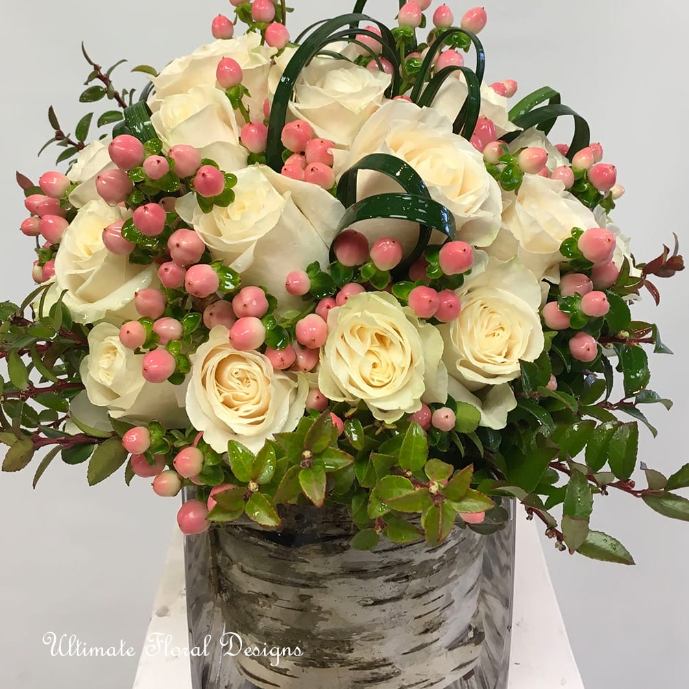 White rose arrangement with pink berries in a glass vase