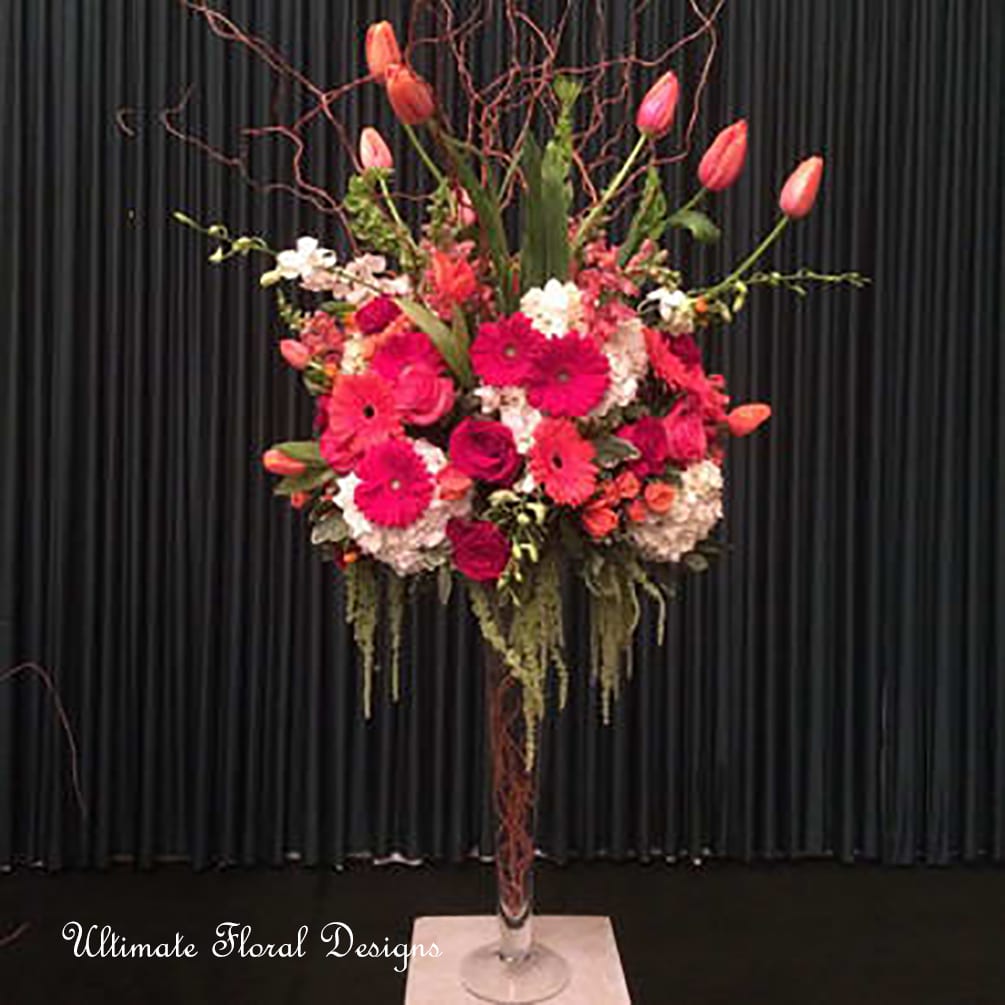 Tall floral arrangement with pink tulips and bright gerbera daisies in a glass vase