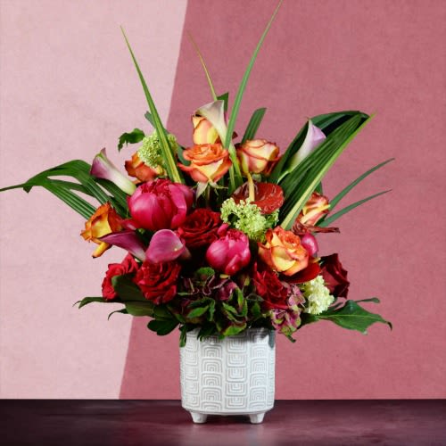 Mixed bouquet of red, pink, and orange flowers in a white vase