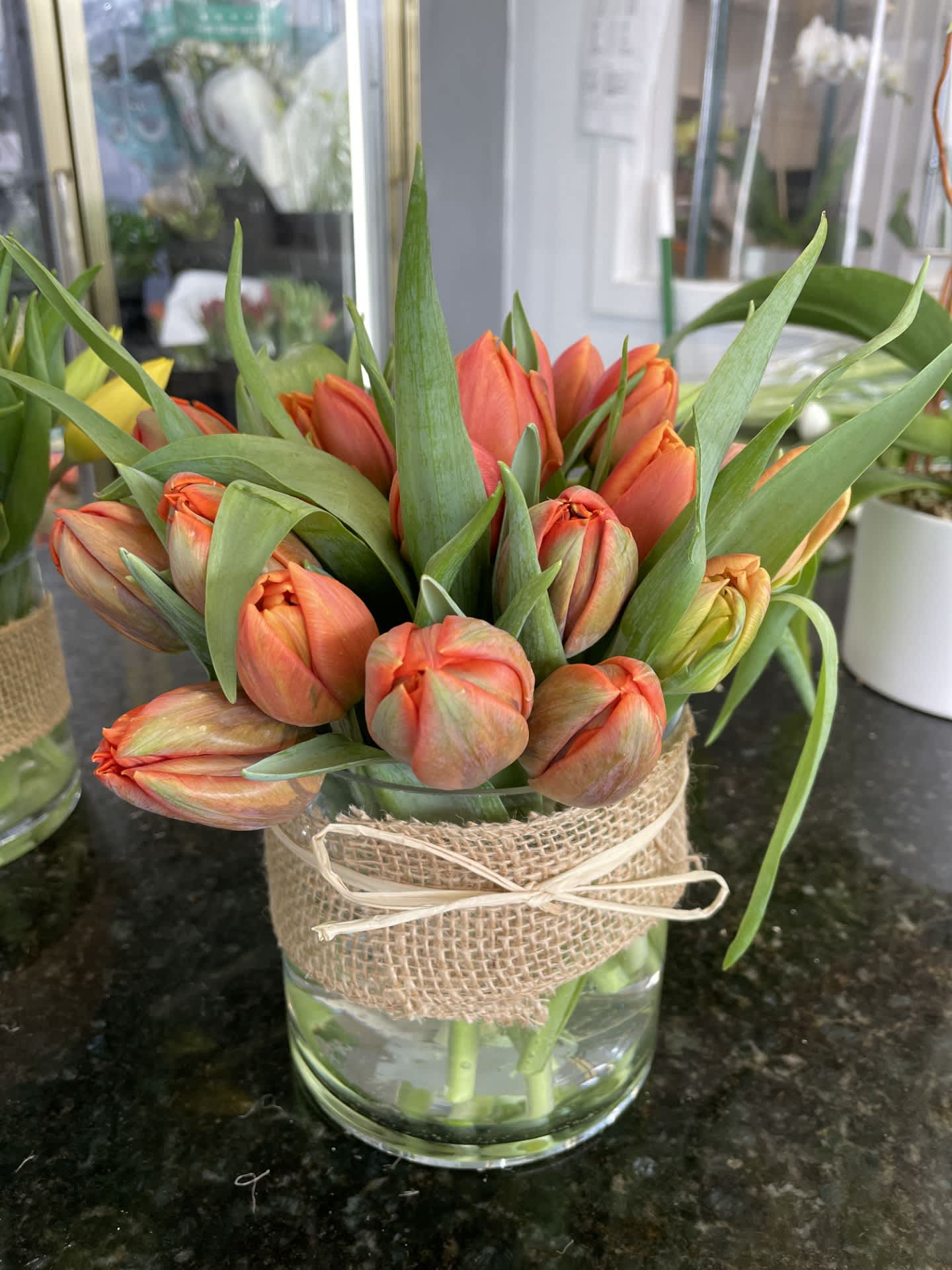 Orange tulip bouquet in a glass vase wrapped with burlap and ribbon