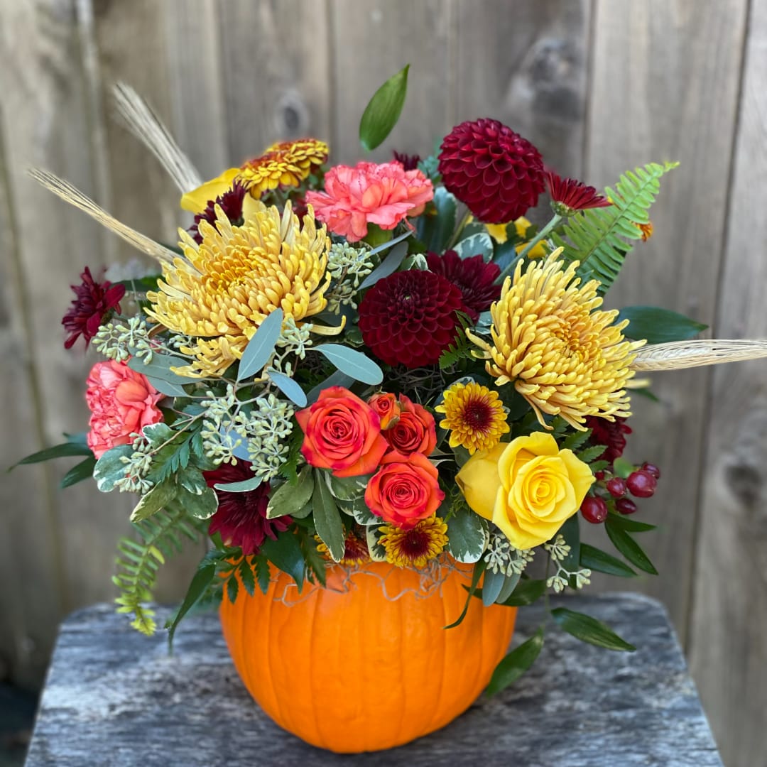 Mixed bouquet in an orange pumpkin container with yellow, red, and pink blooms