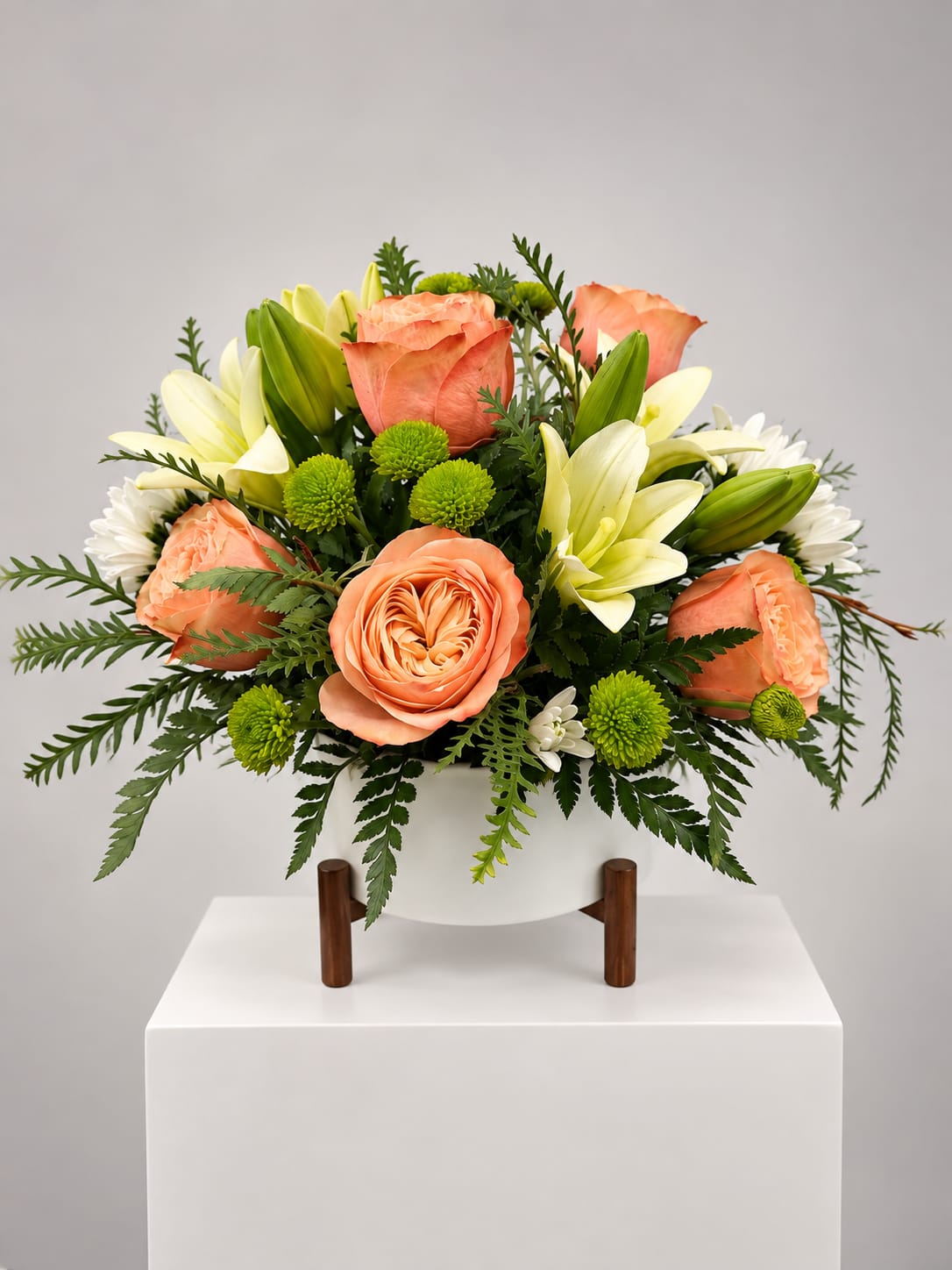 Peach roses and white lilies arranged in a white vase