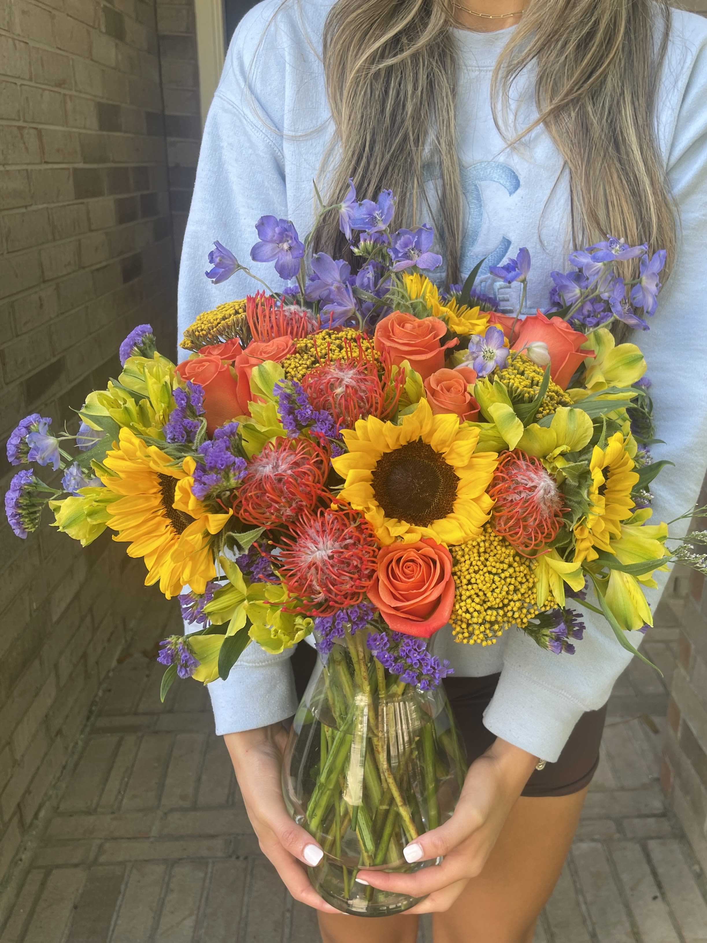 Bright mixed bouquet with sunflowers, orange roses, and purple flowers in a glass vase