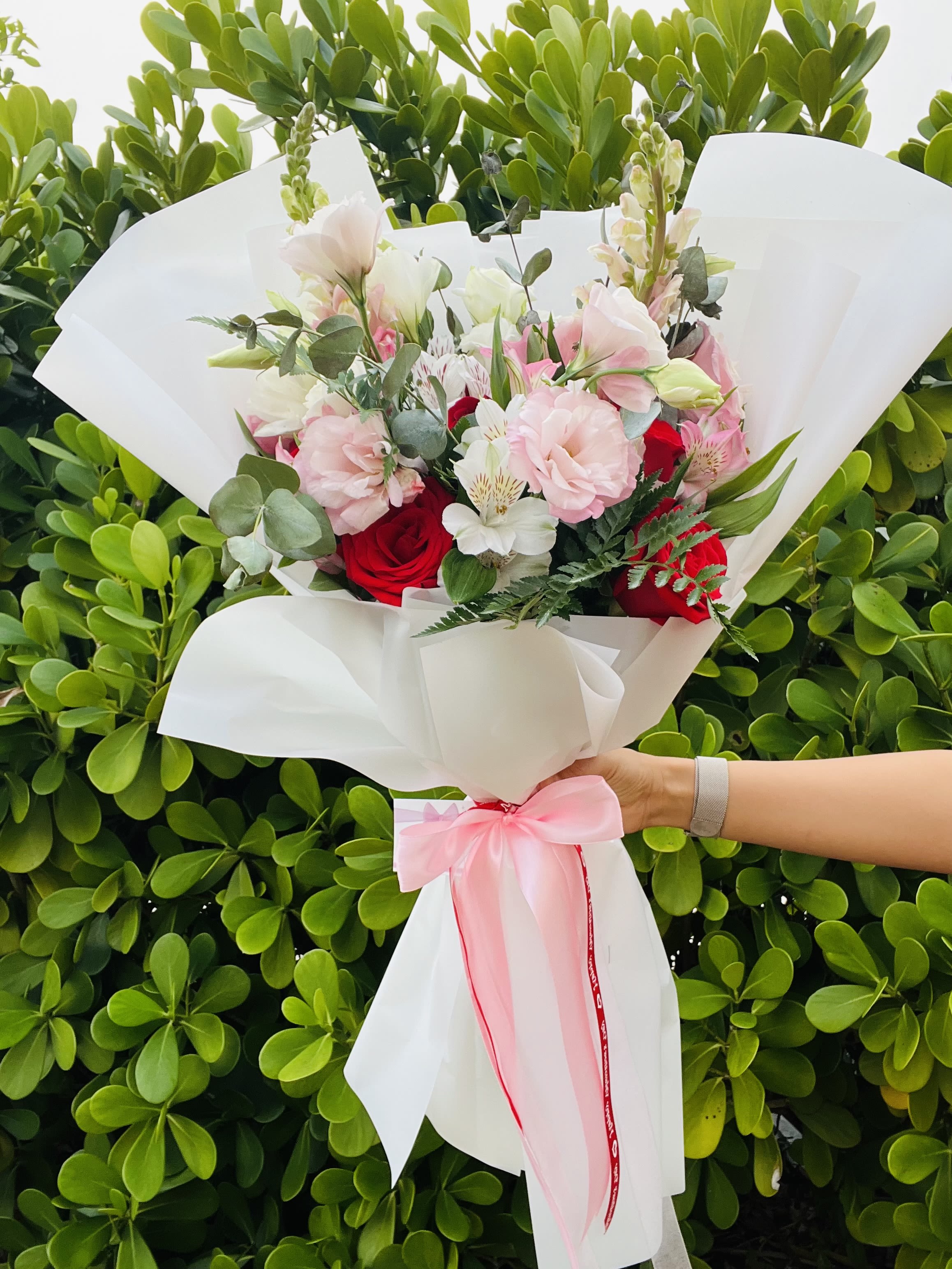 Bouquet of pink and red flowers wrapped in white paper with a pink ribbon